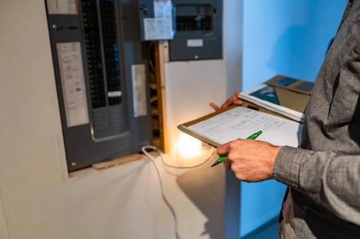 A man inspecting a home's electrical panel; he's holding a clipboard and pen.